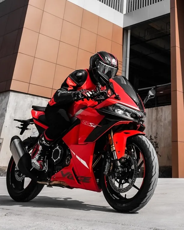 Rider posing with the red VOGE 525RR motorcycle near a modern building.