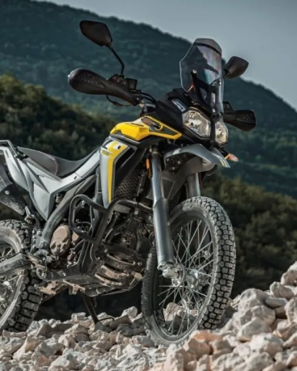 Voge 300 Rally motorcycle riding off-road on rocky terrain with mountains in the background.