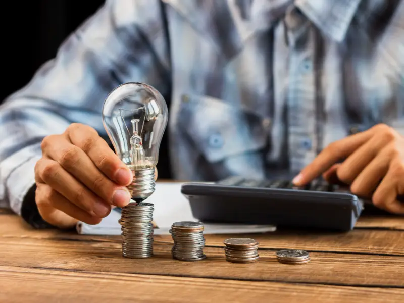 Light bulb balanced on stacked coins near calculator, representing innovation and finance