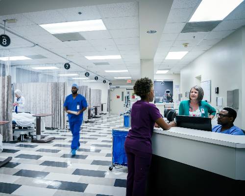 Hospital nurses and staff at nurses' station with patient rooms in background