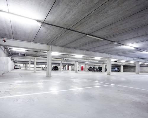Empty concrete parking garage with white floors and fluorescent lighting