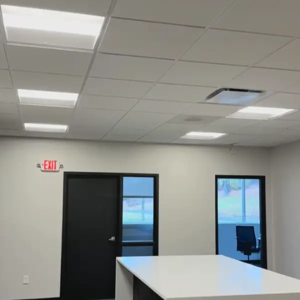 Empty office room with white walls, fluorescent lights, and exit sign