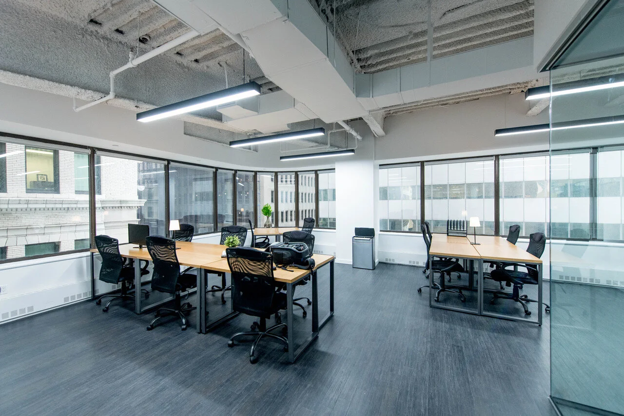 Modern open-plan office with wooden tables, black chairs, and large windows
