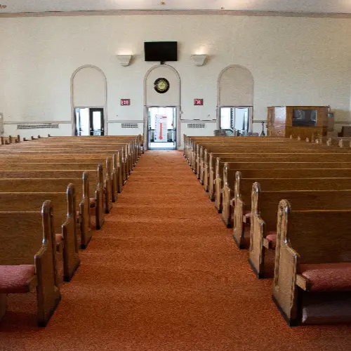 Empty church interior with wooden pews and red carpet leading to entrance
