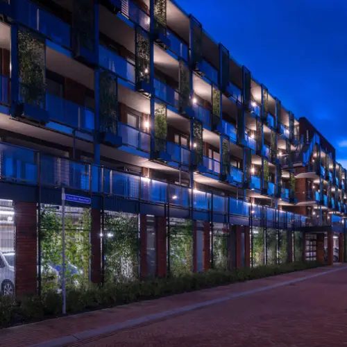 Modern apartment complex illuminated at night with blue lighting and greenery