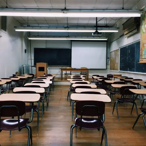 Empty classroom with desks, chairs, blackboard, and projector screen