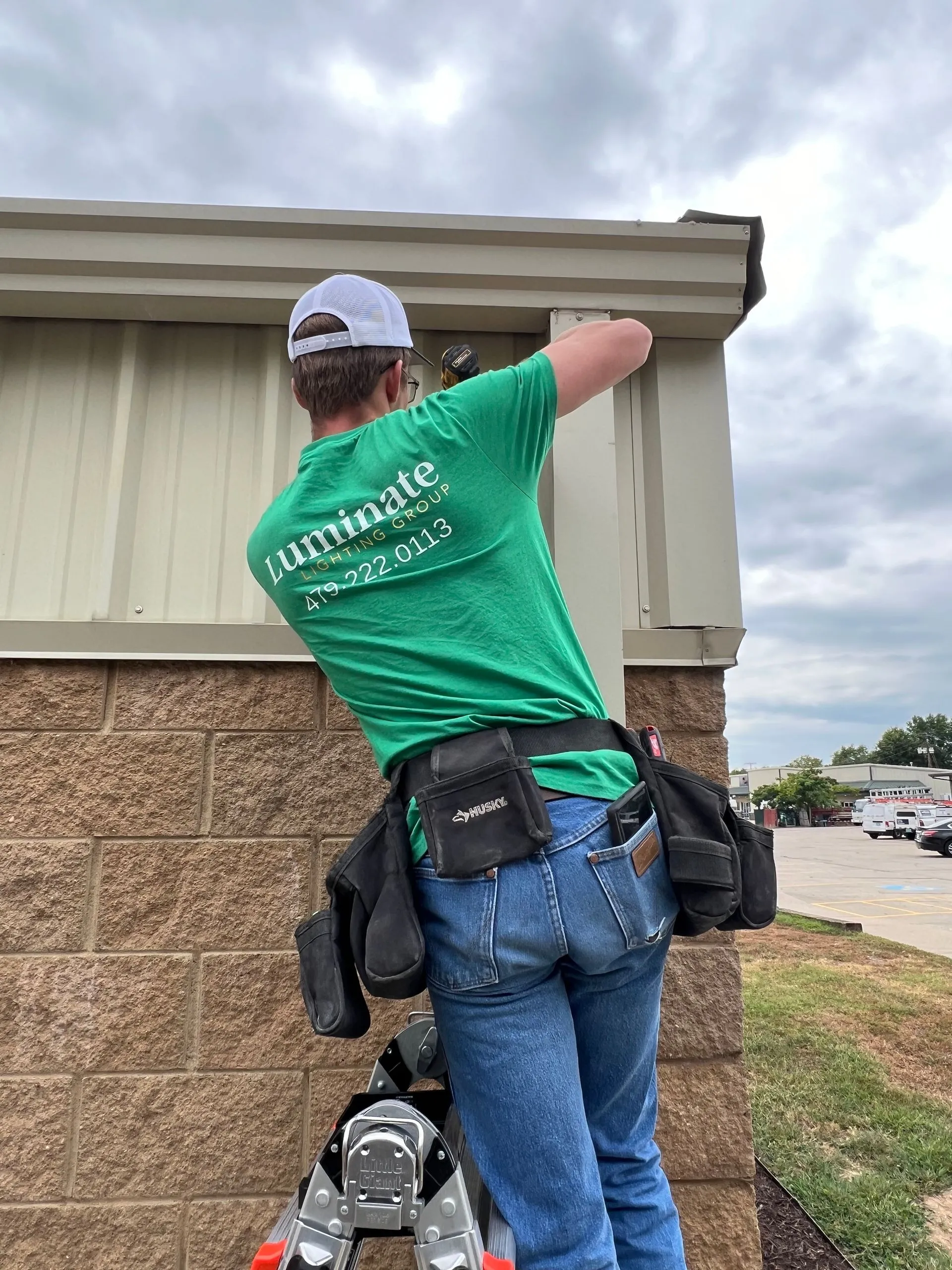 Worker in green Luminate shirt installing or repairing equipment on building wall