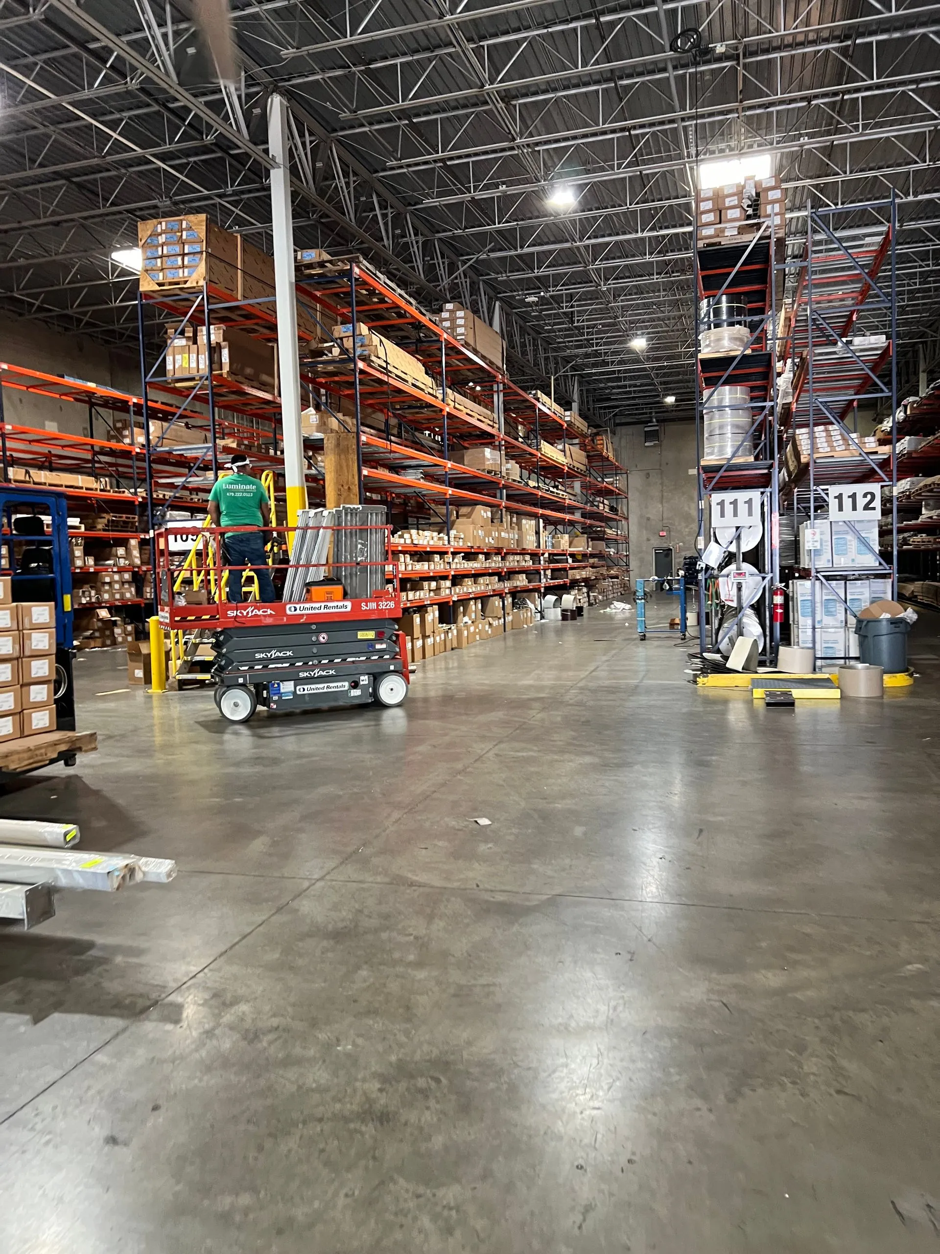 Warehouse interior with tall shelves, worker on scissor lift, and inventory boxes