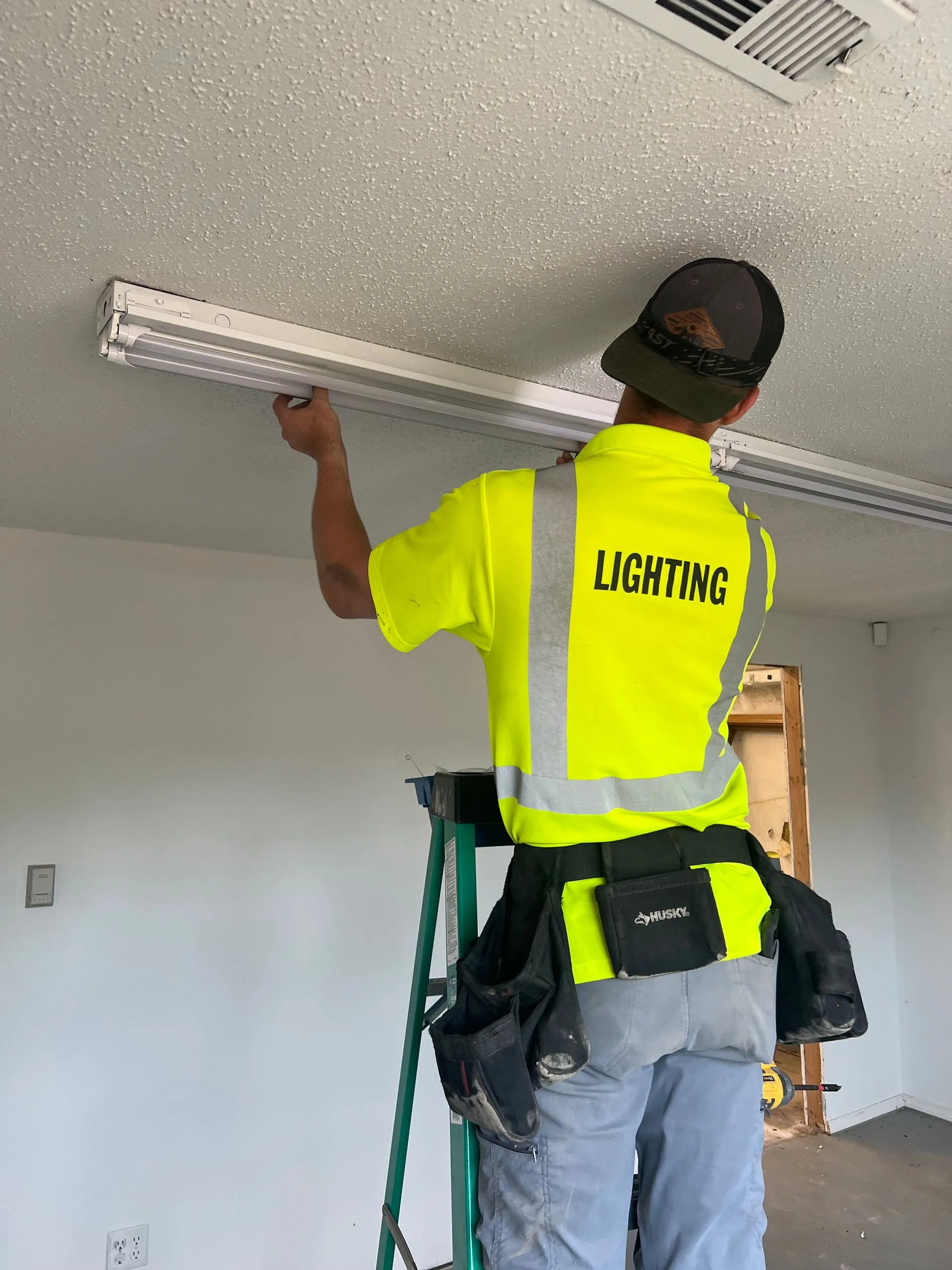 Worker in safety vest installing fluorescent light fixture on ceiling