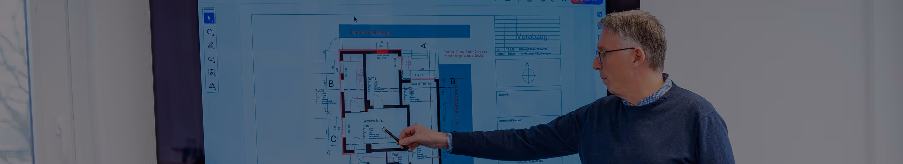 Ein Mann zeigt auf einen Bauplan, der auf einem großen Bildschirm dargestellt ist.