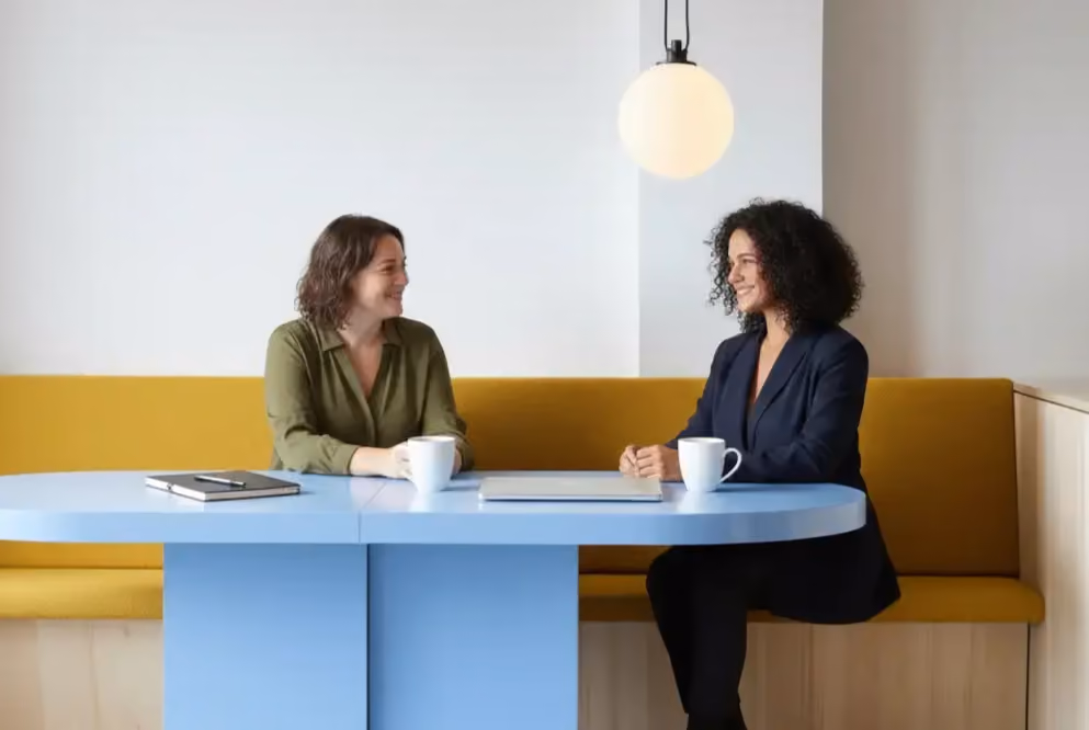 Two colleagues chatting over coffee at a blue table