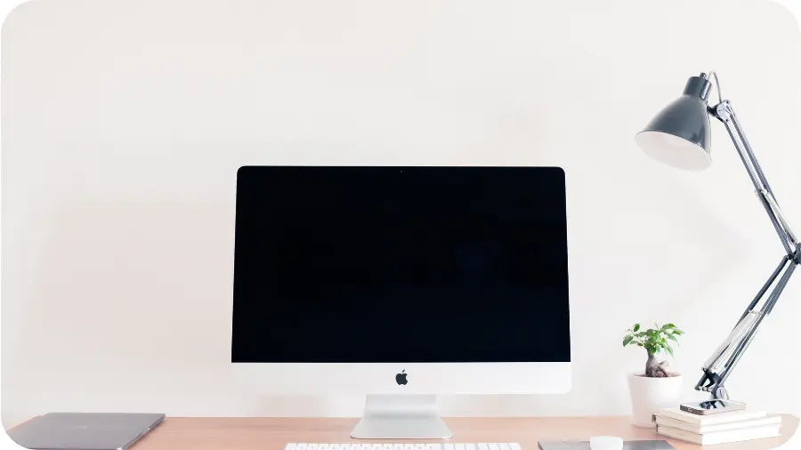 A computer on a desk with a lamp and plant