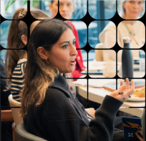 Young woman with long hair speaking passionately during a meeting with colleagues around a table.