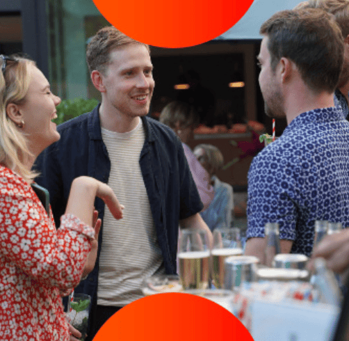 Three people socializing and smiling outdoors near a table with drinks.