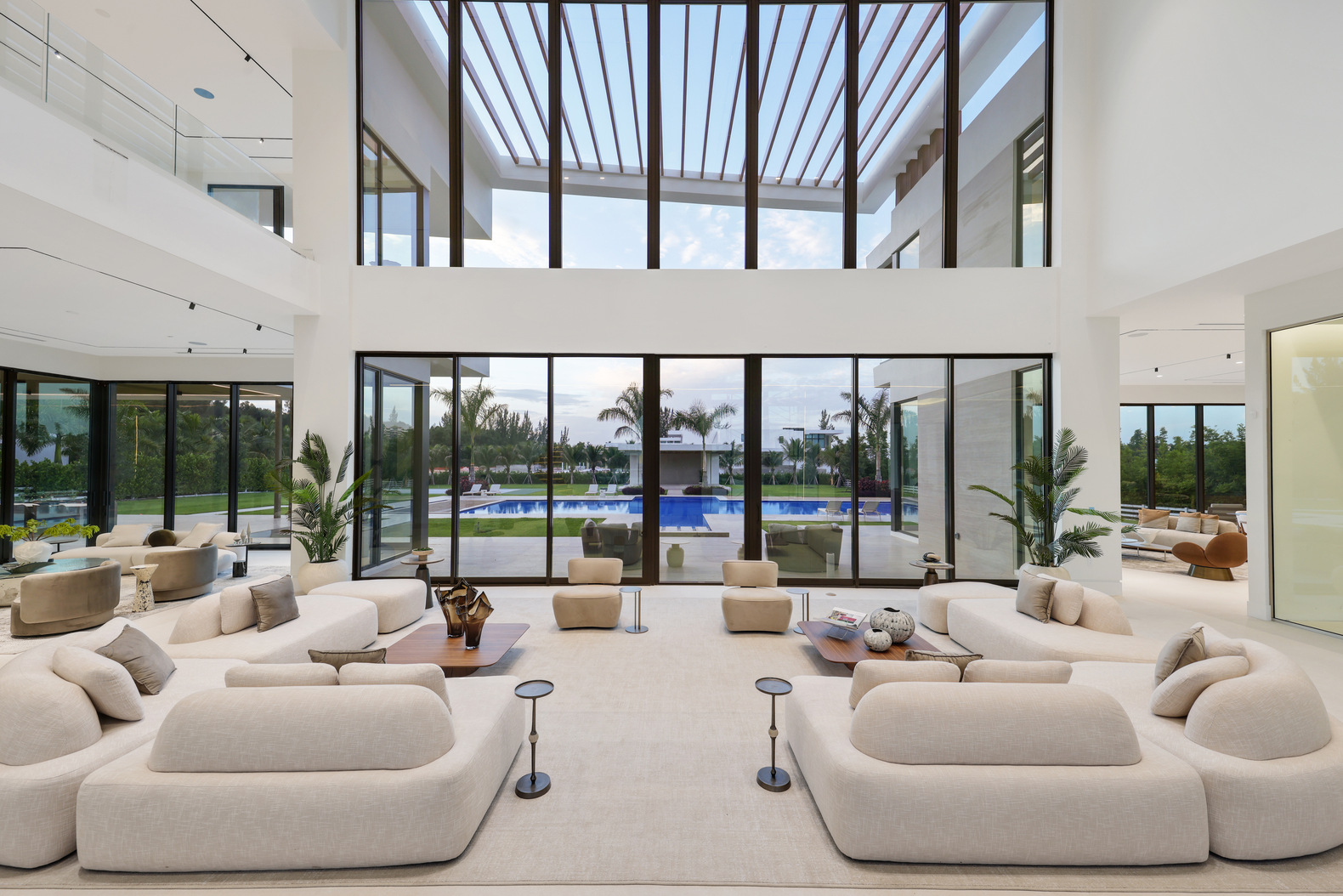 Modern spacious living room with large windows overlooking a pool and garden outside.