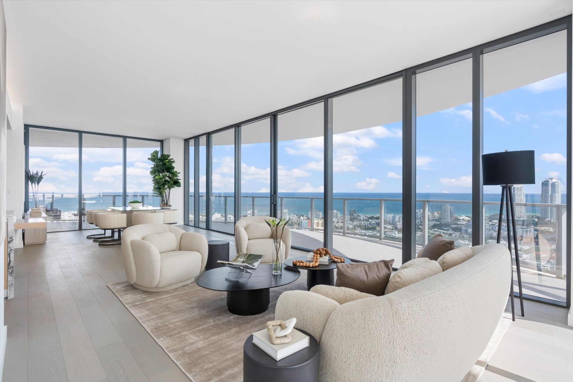 Modern living room with cream seating, large windows, ocean view, and dining area in background.