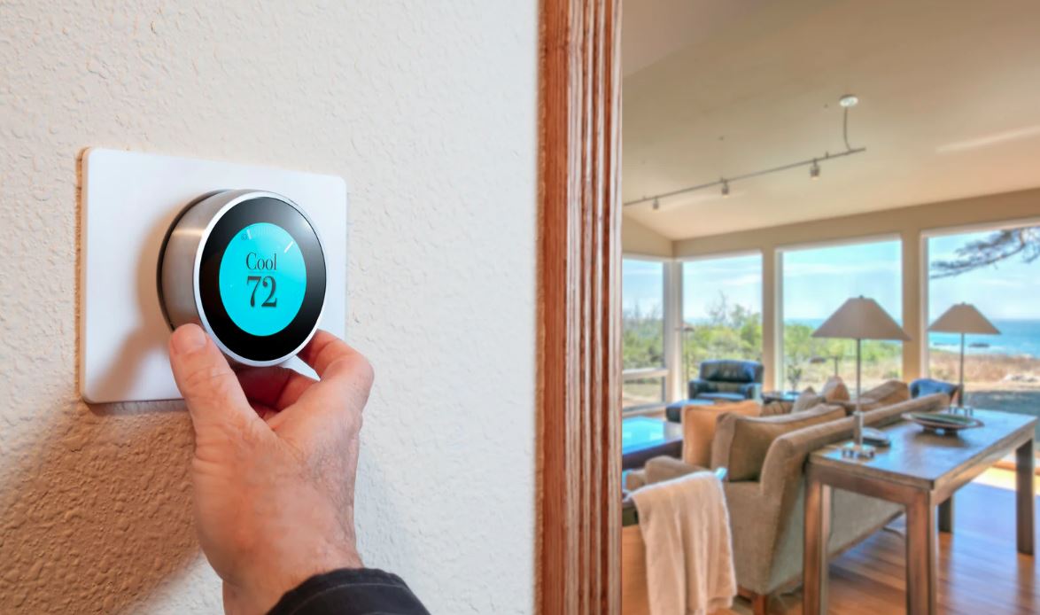 Hand adjusting a smart thermostat set to 72 degrees in a bright living room.