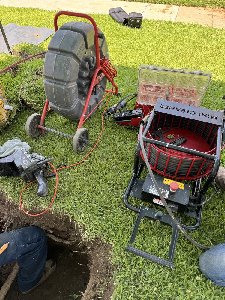 Plumbing equipment and drain-cleaning tools set up beside a dug hole in a lawn.