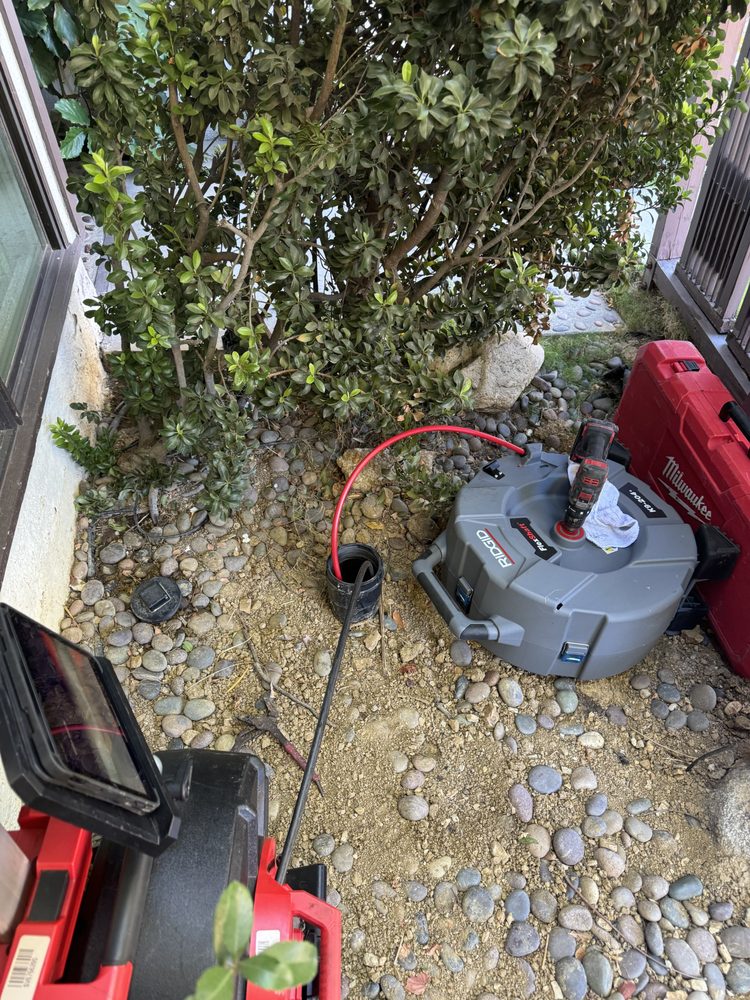 Plumbing equipment and drain-cleaning tools set up beside a dug hole in a lawn.