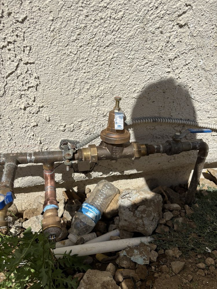 Outdoor plumbing pressure regulator installed on a wall with exposed piping.