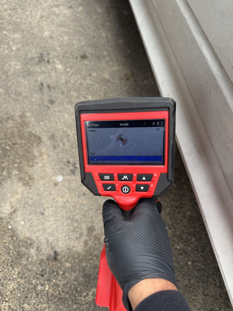 Hand holding a pipe-locating device displaying a signal on the screen.