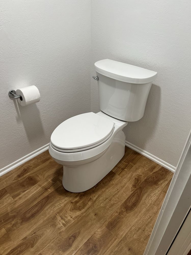 Clean white toilet installed in a small bathroom with wood flooring.
