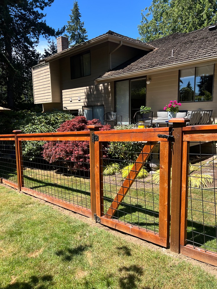 Modern hog wire fence with a wooden gate enclosing a landscaped backyard of a suburban home