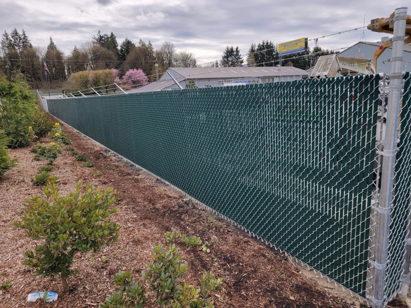 Commercial chain-link perimeter fence with green privacy slats and angled barbed-wire arms