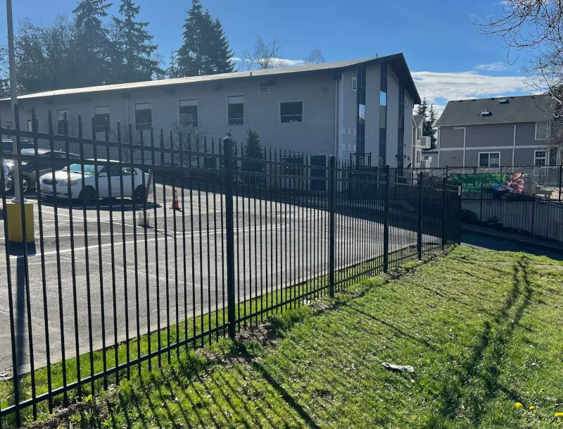 Black ornamental steel fence with spear-top pickets securing a commercial parking lot