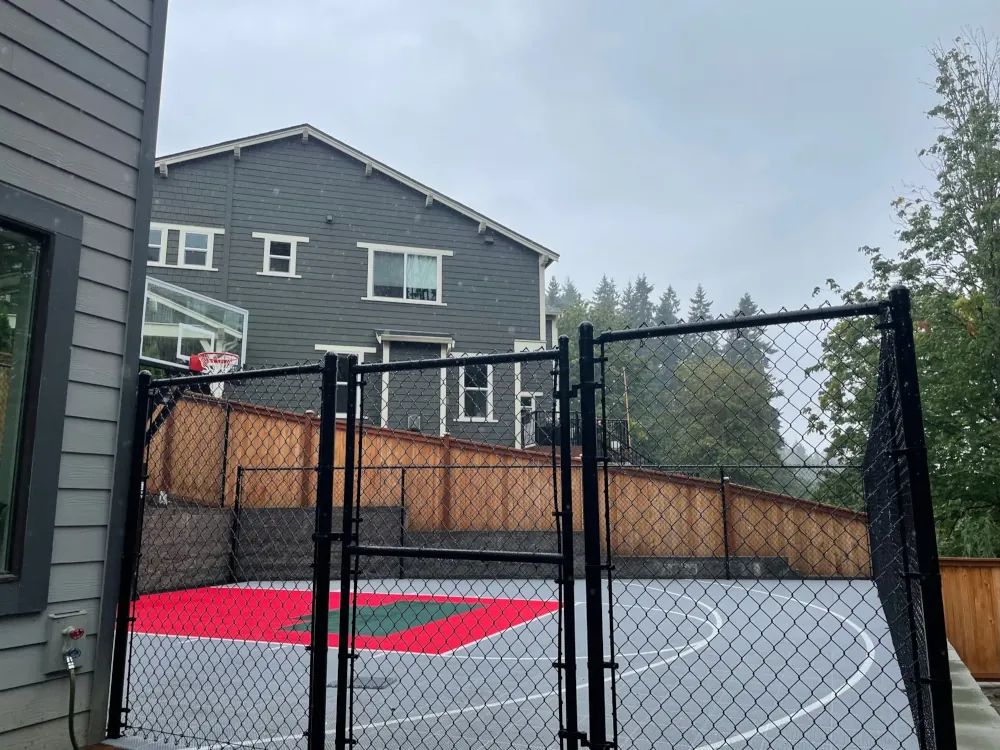 Black chain-link fence with double swing gate enclosing an outdoor sport court