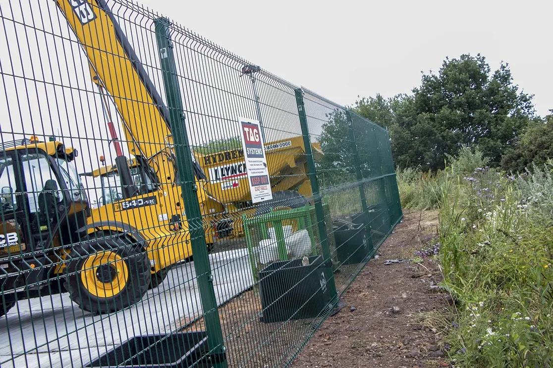 Green welded wire temporary security fencing with weighted bases and “Keep Out” sign enclosing heavy equipment at a construction site