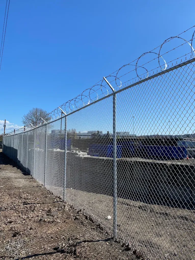 High security galvanized chain link fence topped with razor wire coils along an industrial property line.
