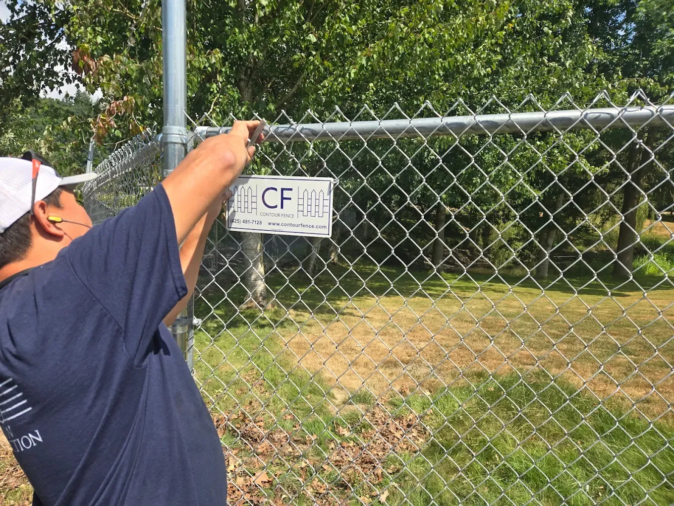 Close-up of a worker attaching a company sign to a galvanized chain link fence.