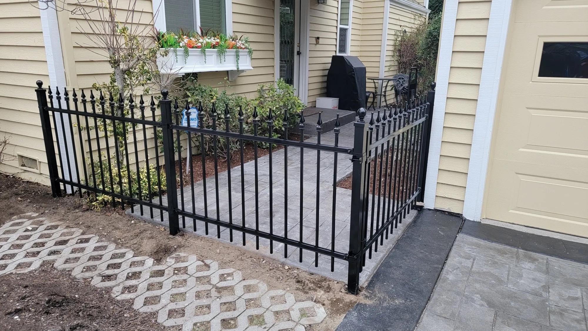 Black wrought iron-style fence with pointed finials installed along a paver patio entryway.