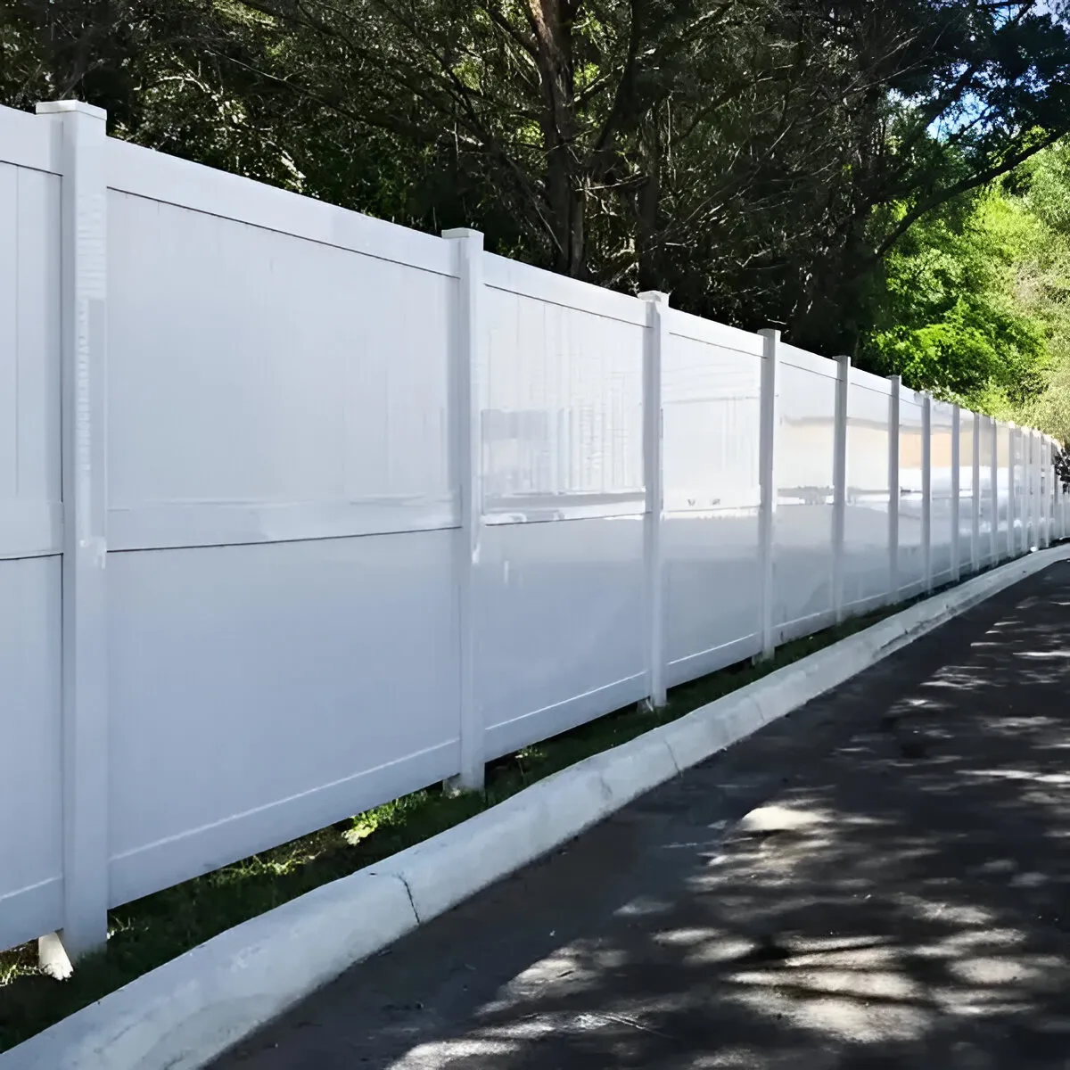Long white vinyl privacy fence with post caps installed beside an asphalt driveway.