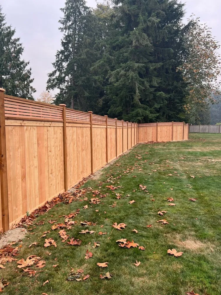 Tall natural wood privacy fence with a framed horizontal slat top accent running along a grassy backyard.