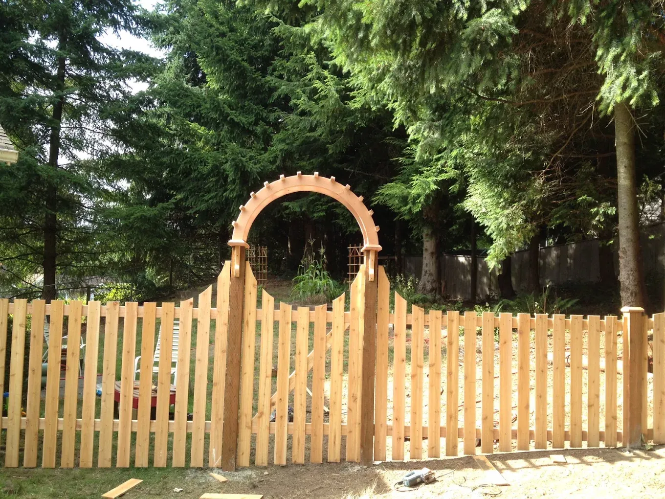 Spaced wood picket fence with flat-top boards and a center gate topped with a decorative wooden arch.