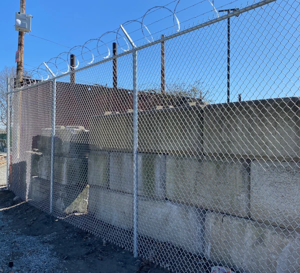 Commercial chain link security fence topped with razor wire and barbed wire surrounding stacked concrete block retaining wall.