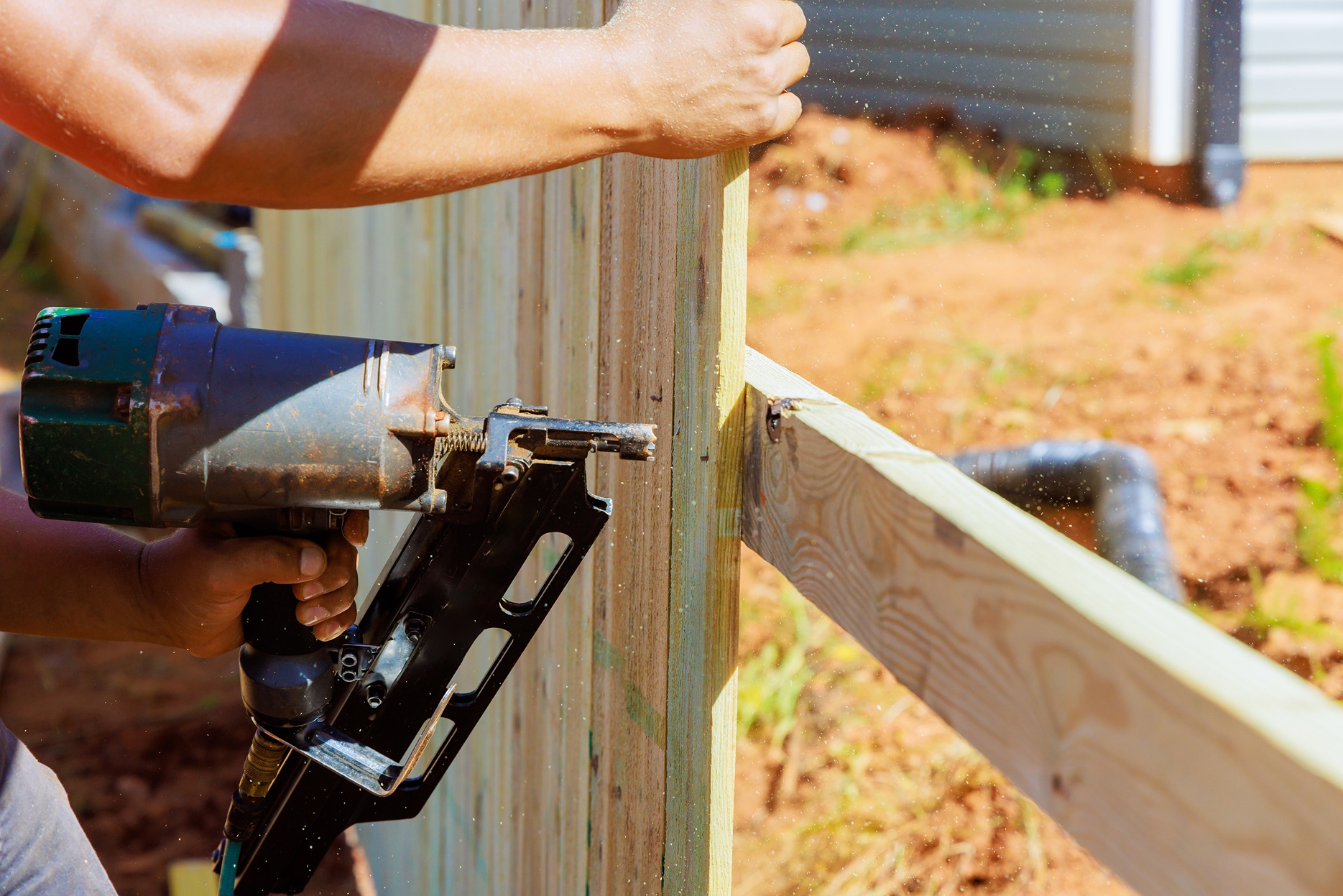 Professional installing a fence section using an air nail gun
