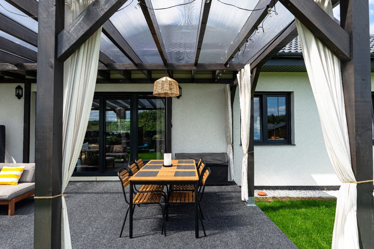 Covered patio dining area under a pergola with curtains for shade and privacy
