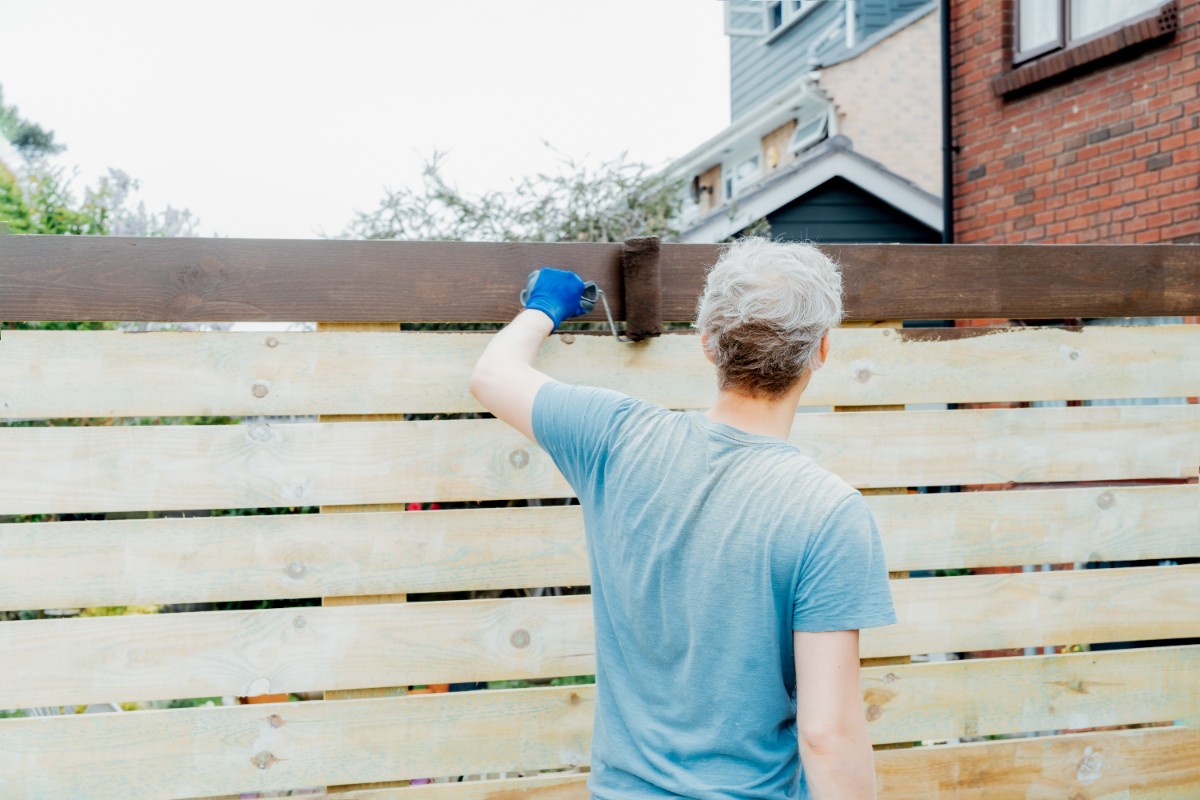 A fence contractor applying stain on wooden fence in Seattle using a roller