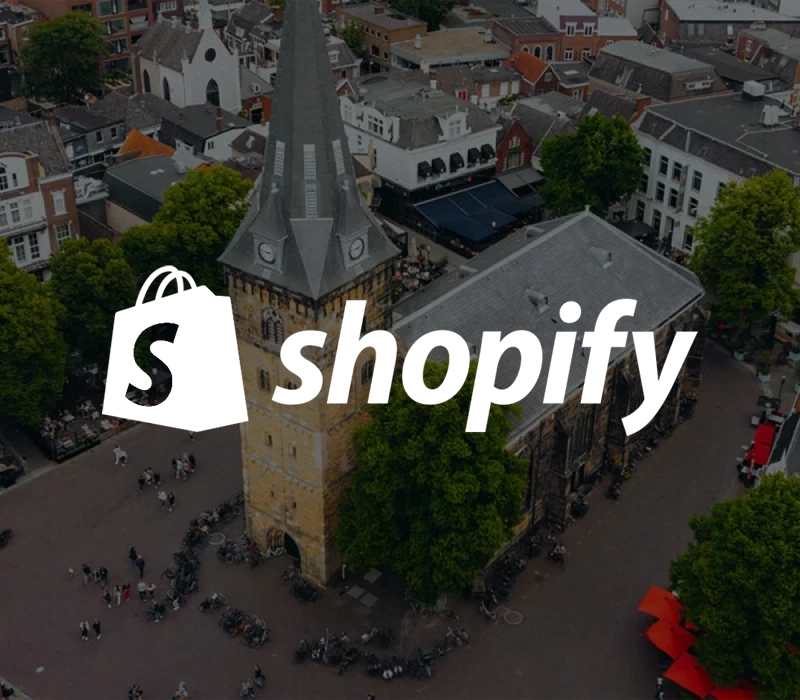 Het shopify logo met op de achtergrond de oude markt van Enschede