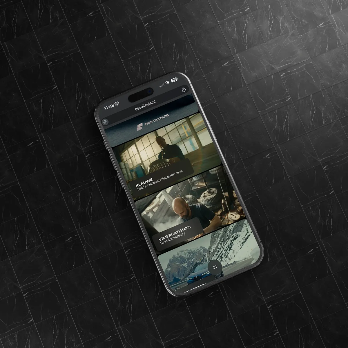 Smartphone met portfolio website van Ties Olthuis waarop videoprojecten worden getoond, liggend op een donkere marmeren tegelvloer.