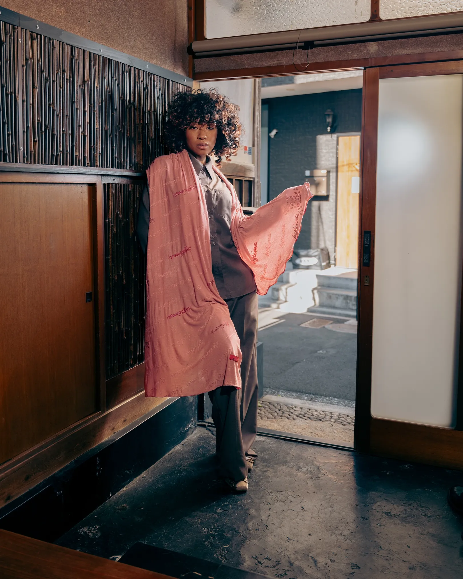 Model poseert in traditionele Japanse woning met roze BYLIMA sjaal en grijs pak bij open schuifdeur.