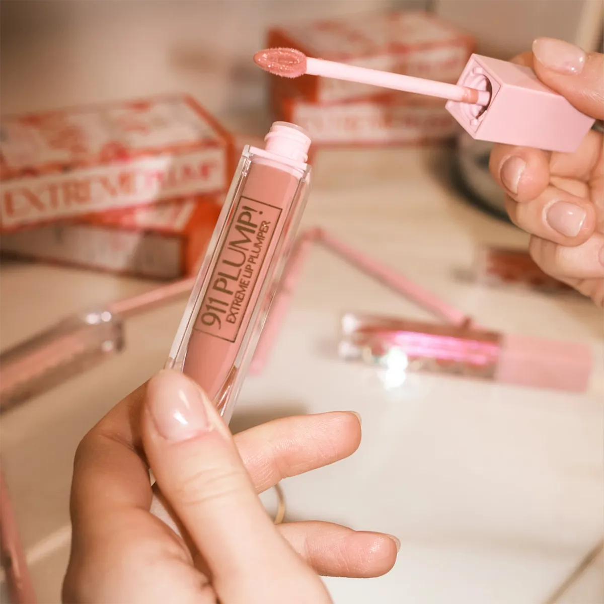 Close-up van BYLIMA 911 Plump Extreme Lip Plumper lipgloss in roze tint met applicator en verpakkingen op de achtergrond.