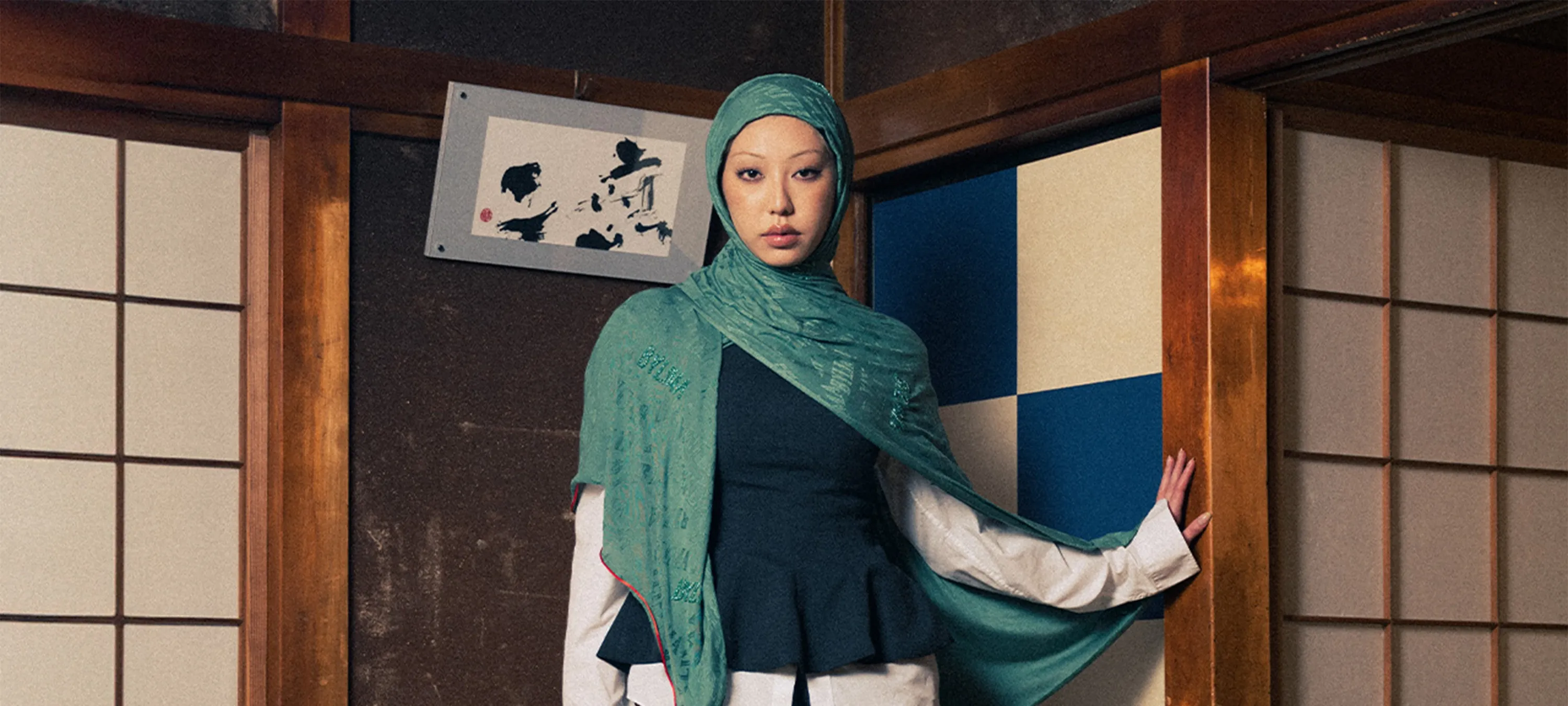 Vrouw met groene BYLIMA hijab poseert in traditioneel Japans interieur met houten schuifdeuren en kalligrafiekunst op de achtergrond.