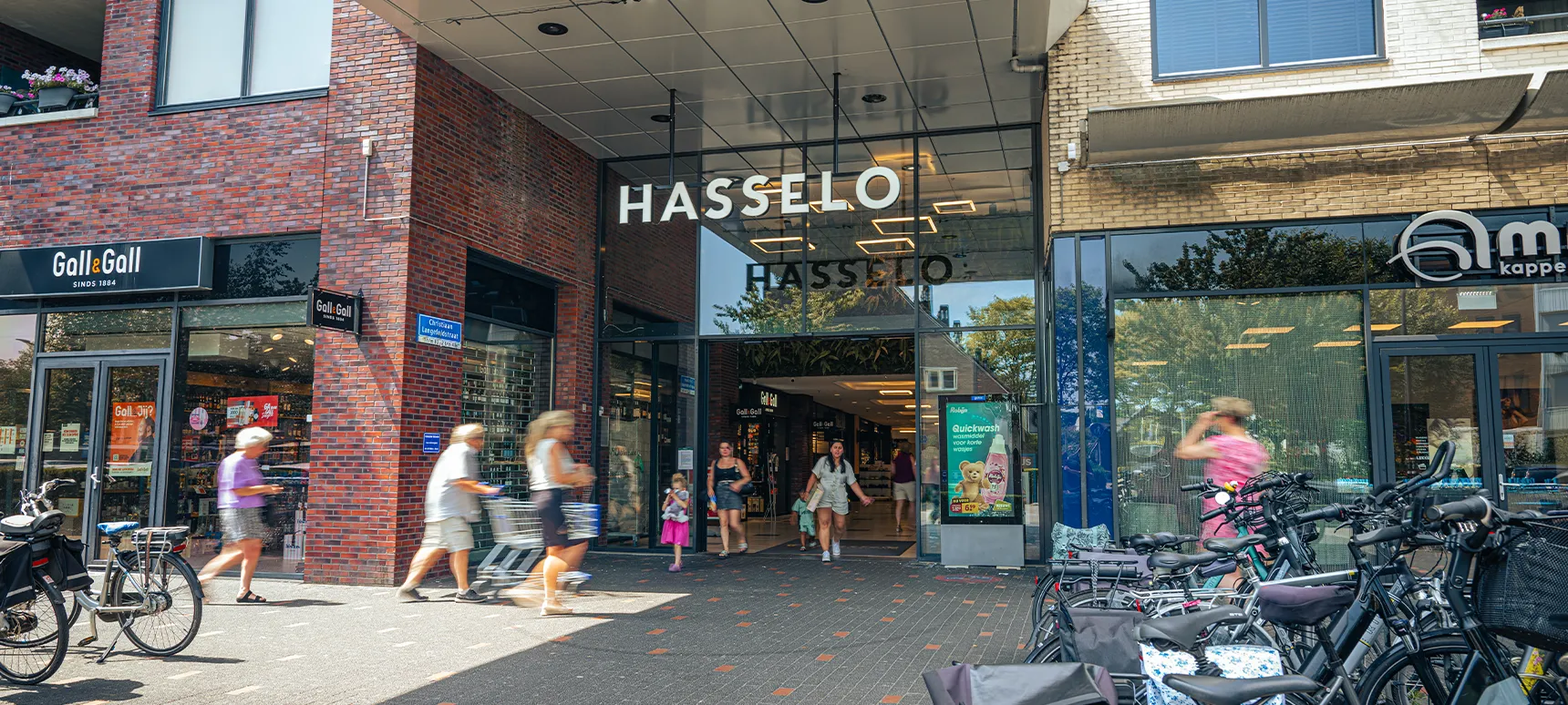 Entree van Winkelcentrum Hasselo in Hengelo met winkelend publiek, fietsen en de winkel Gall & Gall.