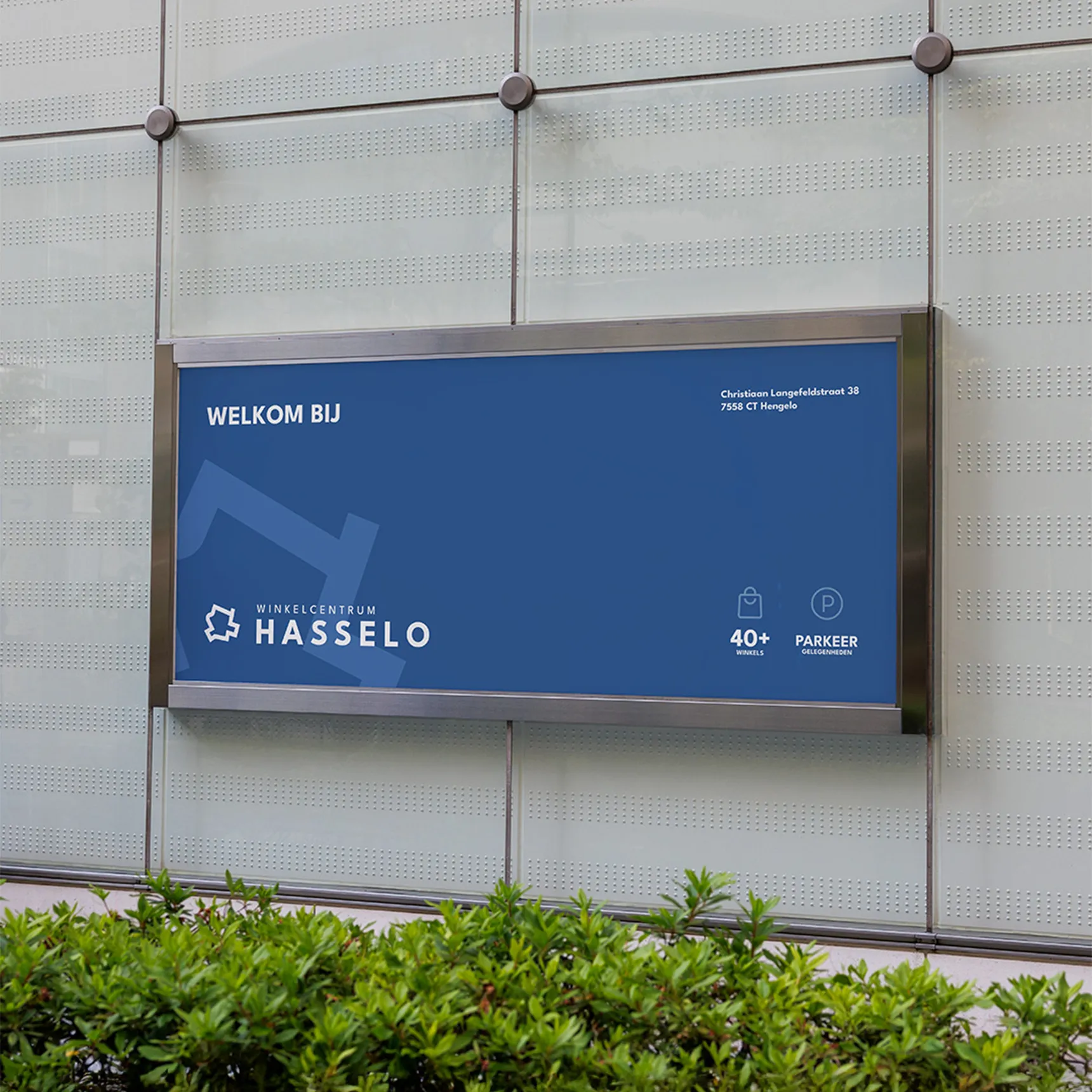 Blauw welkomstbord van Winkelcentrum Hasselo aan de gevel, met adres, aantal winkels en parkeergelegenheden.