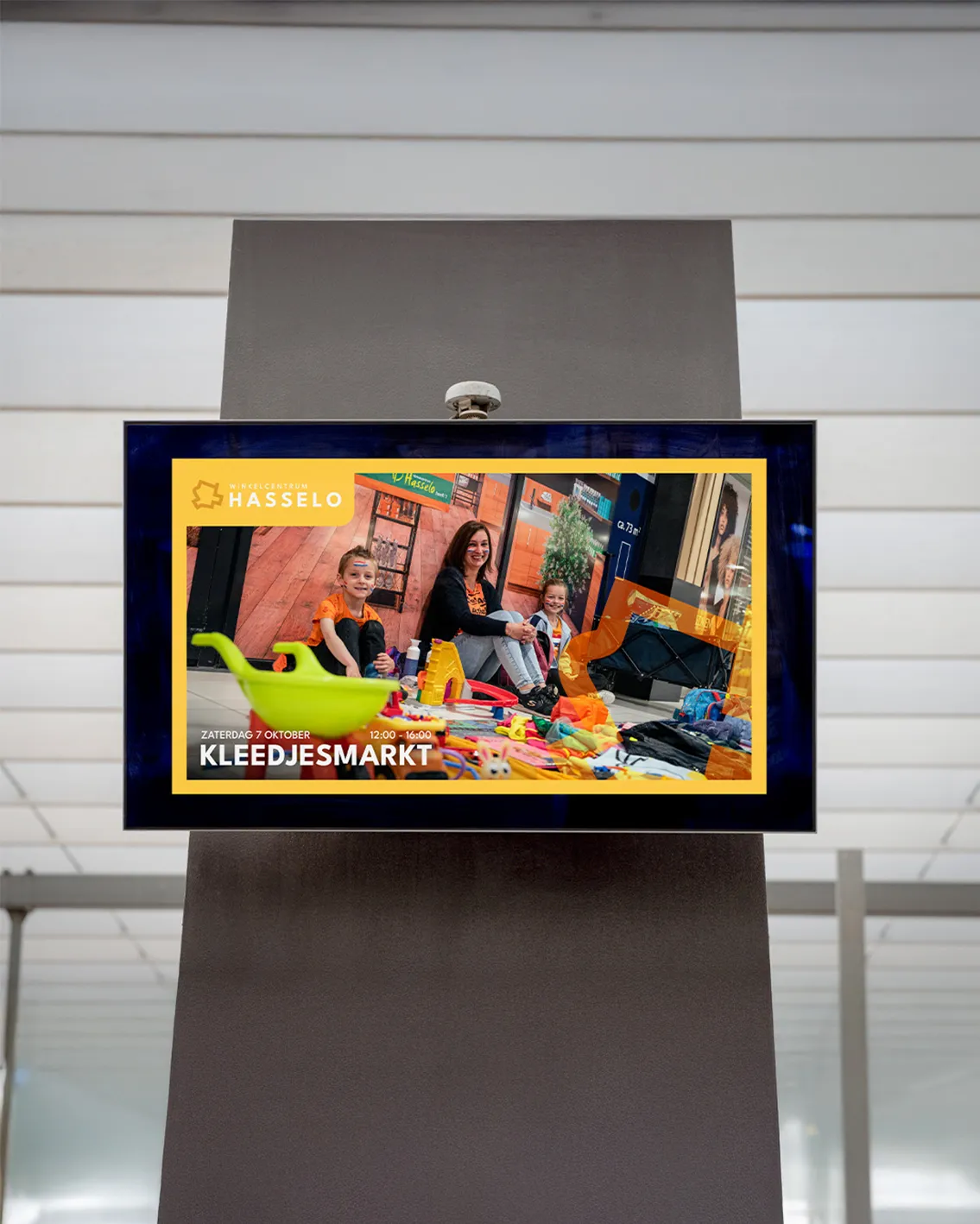Digitaal scherm in het winkelcentrum met een aankondiging voor de kleedjesmarkt van Winkelcentrum Hasselo.