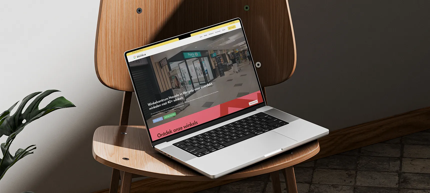 Laptop met de homepage van Winkelcentrum Hasselo op een houten stoel.